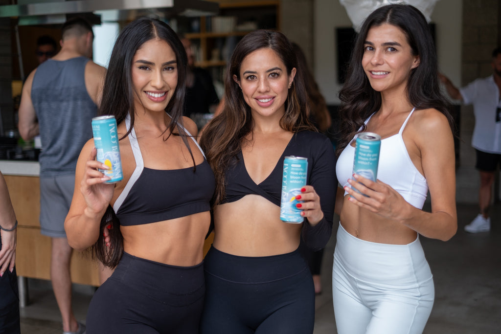 Three women in athletic wear holding Innerbloom cans in an indoor setting